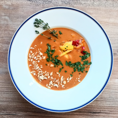die orangefarbene Suppe dekoriert wie beschrieben. Zusätzlich ist noch ein Zweig Thymian an den Rand gelegt.