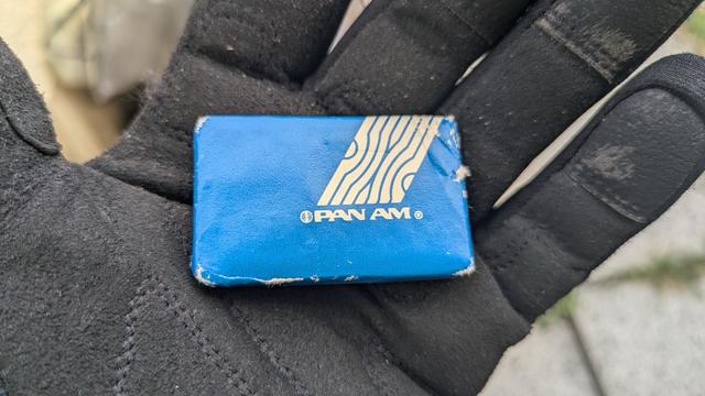 A blue Pan Am branded object, possibly a vintage item, held in a gloved hand. The object shows signs of wear, with scuffed edges and a worn logo. (ai generated)