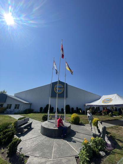 An entrance to a large hangar building with a sign on the facing side that says BC Aviation Museum. It has a yellow float plane on the logo. In front of the building is a round plinth with three flags.