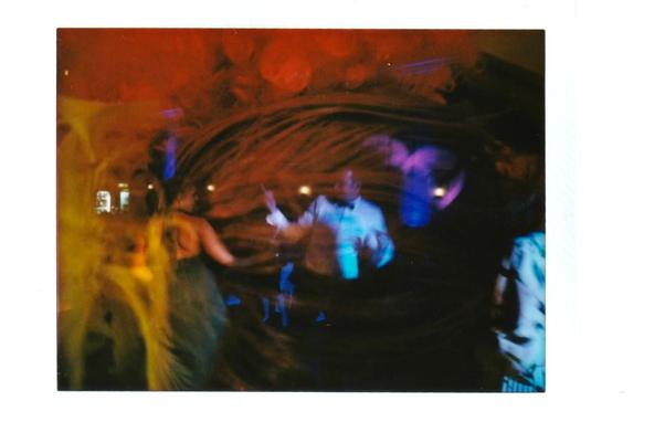 INSTAX colour photo, double exposure: dancing people overlayed by what looks like feathers and wigs