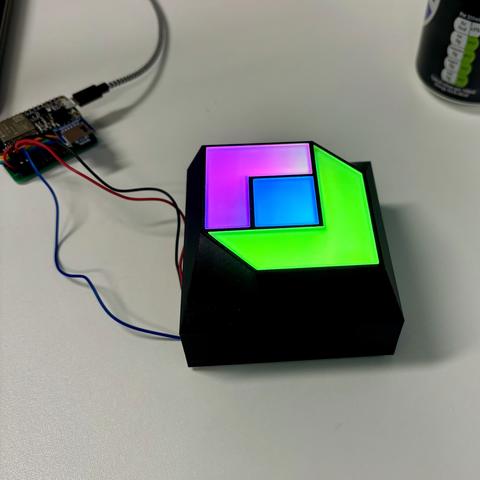 A 3d-printed sign on a desk with 3 lit multicolour segments, next to it is the ESP powering and controlling the LEDs
