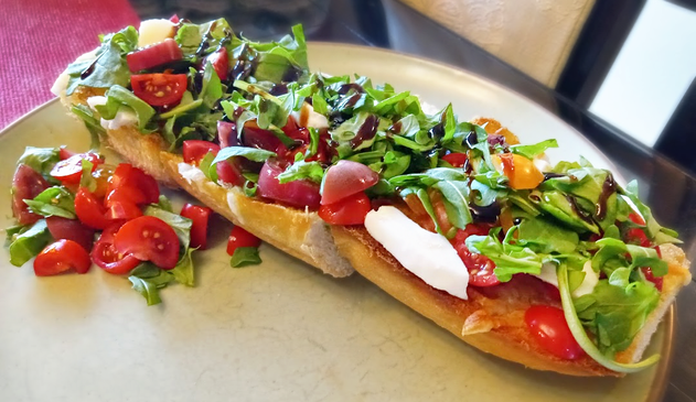 photo of bruschetta on a plate - fresh homemade italian bread toasted with garlic powder and olive oil on top, then topped with fresh mozzarella, fresh sliced cherry tomatoes, arugula, and balsamic glaze
