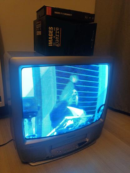 Un combi télévision à tube / magnétoscope sur lequel est posé un coffret de VHS Images de Guerre. Sur la télé, on peut voir Mussolini en train de faire un discours.