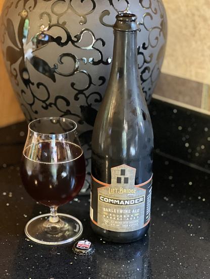 A 750ml bottle next to a snifter glass of ruby red barleywine.