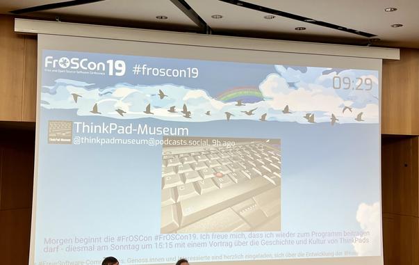 Foto einer Leinwand die Toots mit dem #FrOSCon-Hashtag zeigt - es ist der vorherige Toot dieses Accounts zu sehen