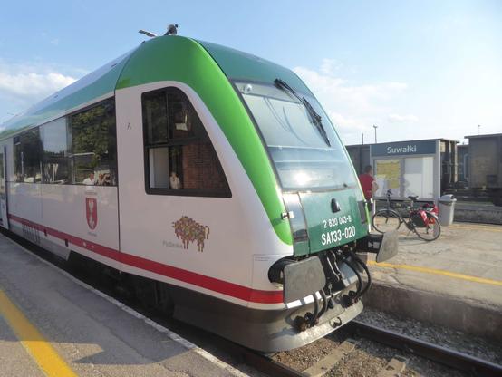 Regional train (diesel) from Białystok arriving in Suwałki. Some bikes get off. Cargo trains (coal?) sitting in the background.