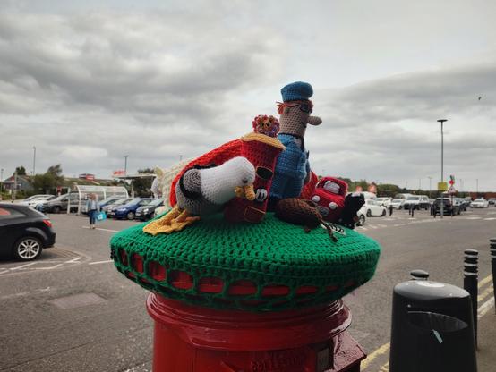 This photo is the other side of the yarn bombed post box showing Postman Pat and his little red car and cat and small crochet post box and a large crochet gull
