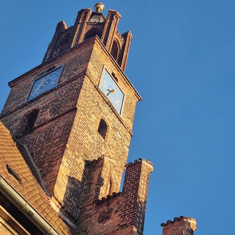 Tower of the Old Town Hall, an imposing brick building. The picture shows the building slightly tilted to the right with the tower's square blue clock faces and parts of the roof.
