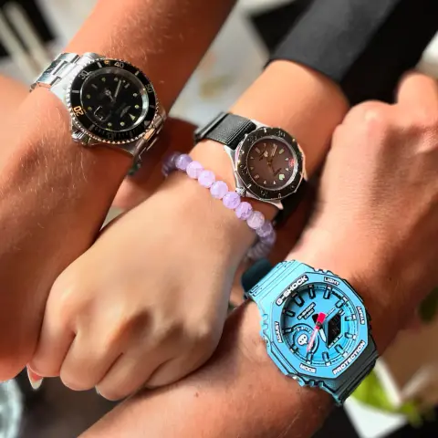 Photo of 3 wrists with watches. Left to right: oldest son with black Invicta quartz dive watch, daughter with pink/purple mother of pearl quartz Seiko dive watch and father with blue manga style Casio Gshock (also called Casio am model)