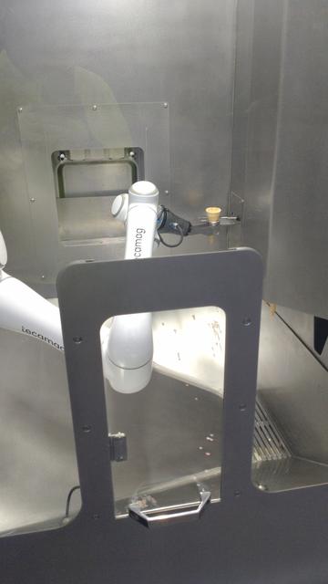 Blick in den Innenraum aus Edelstahl mit weissem Roboterarm.