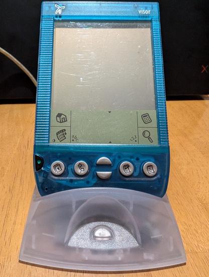 Photo of a translucent blue Handspring Visor PDA resting in a clear syncing cradle. circa 1999