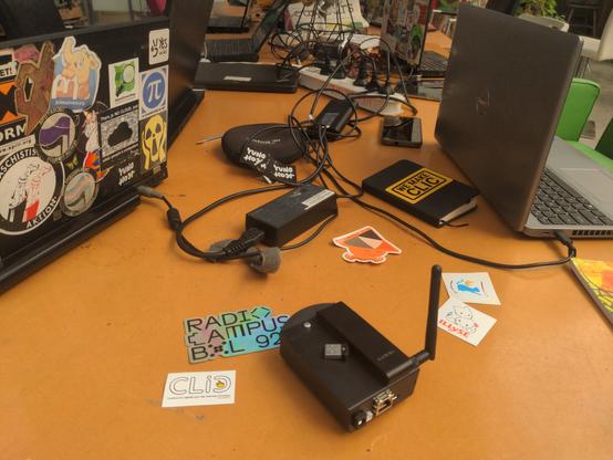 Une table avec quelques ordinateurs portables couverts de stickers, une brique internet en premier plan