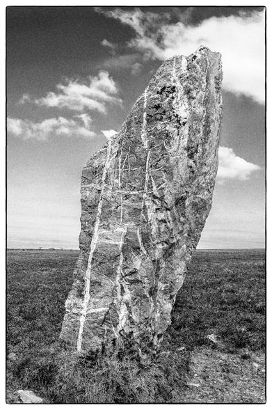A black and white photo of a large standing stone striped with veins of quartz on open moorland.