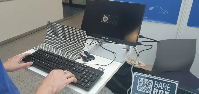 A close up of the hardware demo. It shows a Raspberry Pi Zero 2 W that is connected to a USB keyboard and a HDMI monitor as well as a LED panel connected to the Raspberry Pi by a blue cable as well as a PWM buzzer.