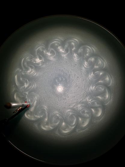 A rotating fluid with vortices. The vortices are created by a stationary pencil partially submerged. The vortices form a ring as the lazy susan spins.