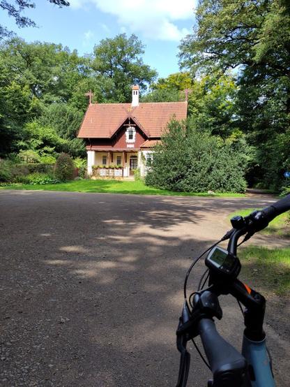 Fahrrad in einem Waldstück mit einem braunroten Haus.