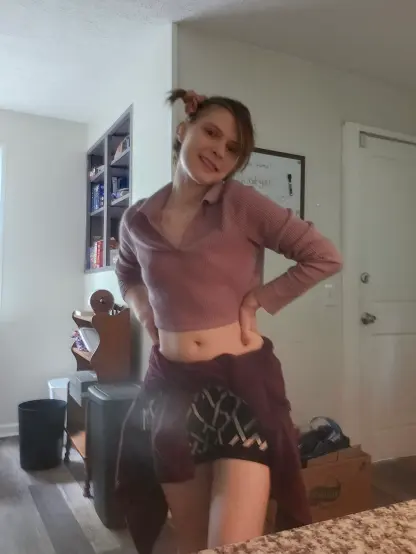 Posed with hands on hips, arms bent, white and black shorts with ice cream cone pattern, white for the stripes. Radish pink Jacket tied around waist. Lavender purple sweater crop-top with collar.  Blonde hair tied to side with pinkish shiny scrunchy. House in background.