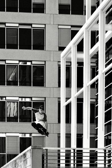 Skater springt von Mauer. Dahinter Gebäude