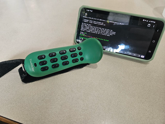 A blue-green one-handed chording keyboard sitting in front of a phone displaying a unix terminal.