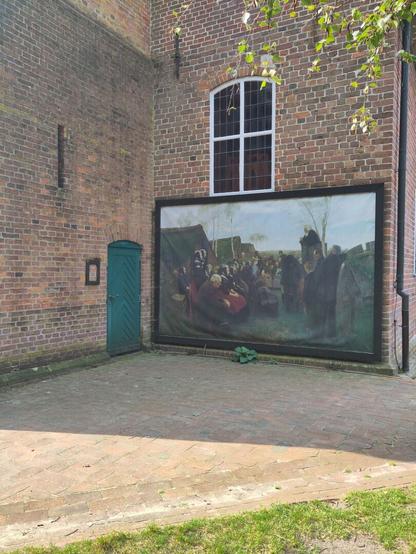 Gebäudeecke, links eine grüne Tür, rechts ein großflächiges Gemälde "Gottesdienst im Freien", darüber ein Fenster.