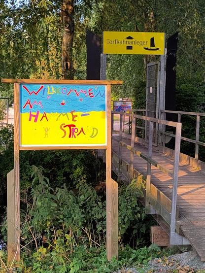 Ein gelb blaues Schild mit der Bezeichnung Hammestrand, dahinter ein weiteres gelbes Schild mit der Bezeichnung Torfkähne.