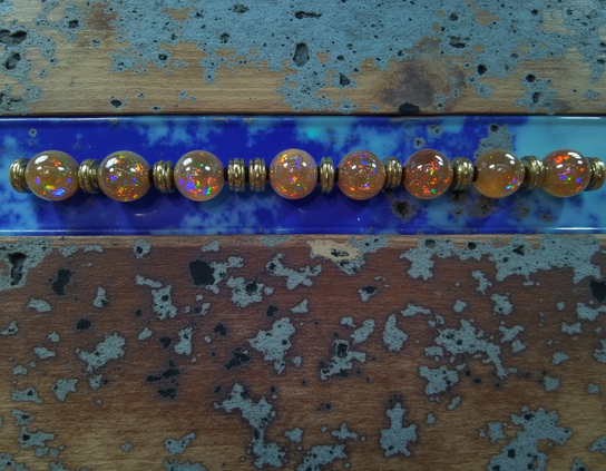 String of opalescent beads with silver spacers on a weathered wooden surface with blue accents, highlighting colorful sparkles and natural textures. Found art style.