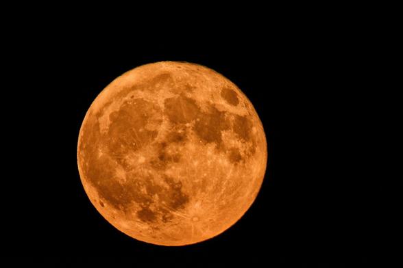 A full moon still close to the horizon, unseen, giving the moon an orange appearance.