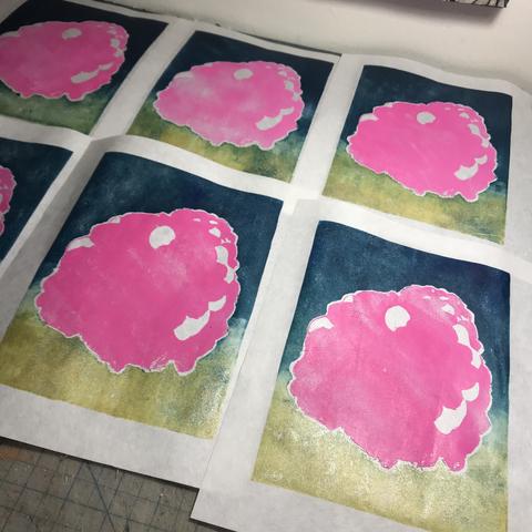 6 linocut prints laid out to dry on a tabletop in two rows of 3, each vertical rectangular printed area with a bulbous pink shape with a few white patches and a background which is a gradient of gold at the bottom to dark teal at the top