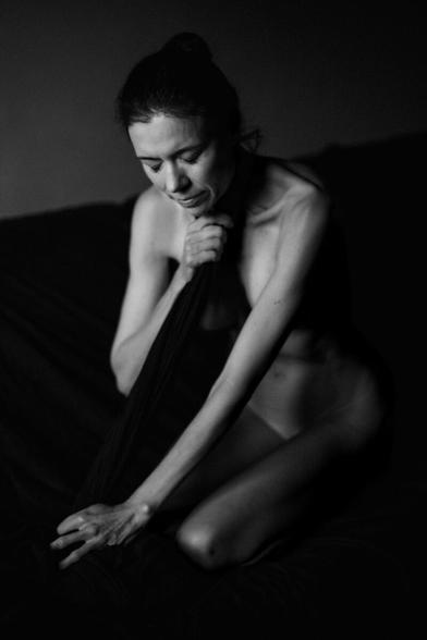 einn schwarzweiss Bild. eine Frau kniet auf einer Couch, sie ist nackt und hat ein schwarzes Tuch um sich und bedeckt die Blöse. Das Tageslicht strahlt sie an und ihre Haut leuchtet, alles andere ist sehr dunkel.
AI disclaimer:
Using my work, its meta data, written or derived description to create media with or train AI based systems is prohibited.
