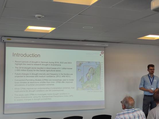 A young man stands in front of a slide summarising a study outline