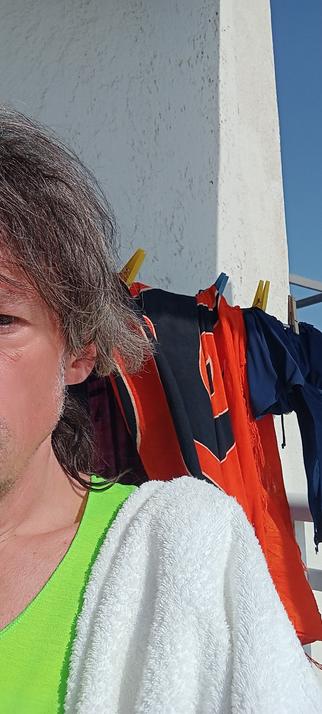 Ein drittel-selfie vom rotbraunen Gesicht daneben ein dünner Streifen "neon"gelbgrünes Shirt, über Schulter weißes Handtuch 
Rot Oranges Strandtuch auf Wand-Wäschetrockner-Rack
Ein wenig weiße Baustruktur, und ein dünner Streifen, etwa 10°, strahlend blauer Himmel