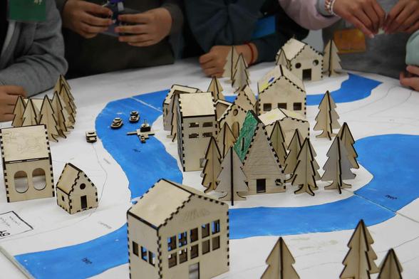 Laser-cut miniature village with rivers and trees. Various size houses, office, and cabins. Kids' hands.