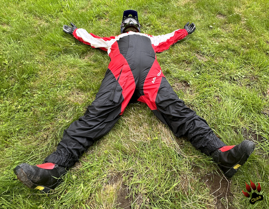 person wearing a red/black/white motorbike rainsuit, Haix boots and a motocross helmet lying on his back in the grass, spread-eagled