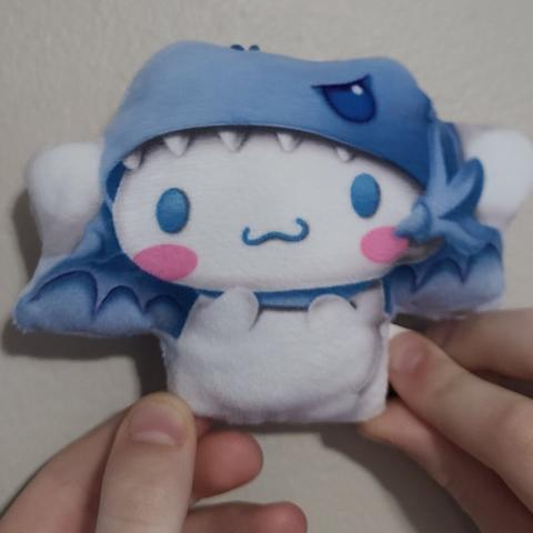 Photograph of two white child's hands holding a small plush figure of Cinnamoroll from Hello Kitty (white puppy with long, floppy ears and large blue eyes) wearing a hood based on the Blue Eyes White Dragon from Yu Gi Oh.