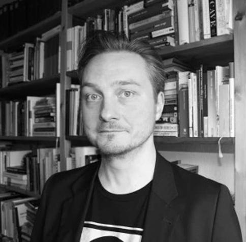 Schwarzweißfoto von Dr. Lars Banhold, der vor einem gut gefüllten Bücherregal steht.