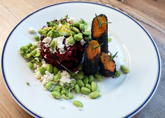 Drei wie Türmchen stehende Stücken Karotte mit Mohn ummantelt. 
Daneben das rote Risotto, bedeckt mit Schafskäsekrümeln + Edamame