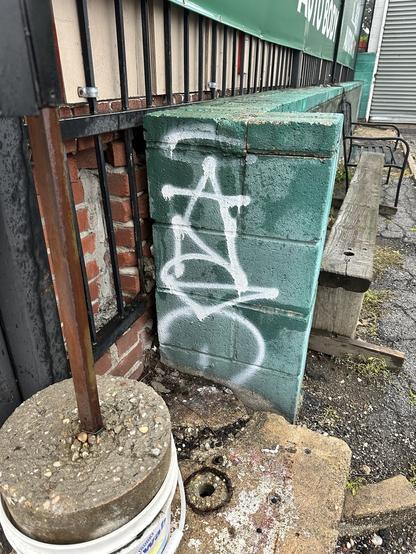 ANSO spraypainted in white vertical letters on a green wall angling into the background of the photo. there's a plastic bucket filled with concrete in the foreground and an unfinished wall behind