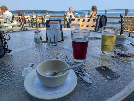 An outdoor dining area at Anthony's Point Defiance. A table in the foreground has two empty clam chowder bowls and two glasses of beer. In the distance is Dalco Passage, part of Puget Sound.