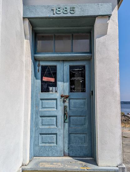 Point Robinson lighthouse. The photo shows the lighthouse door, colored grayish blue. The door is a double door with windows. Above the doorway is a sign that reads "1885" the year the lighthouse was completed.