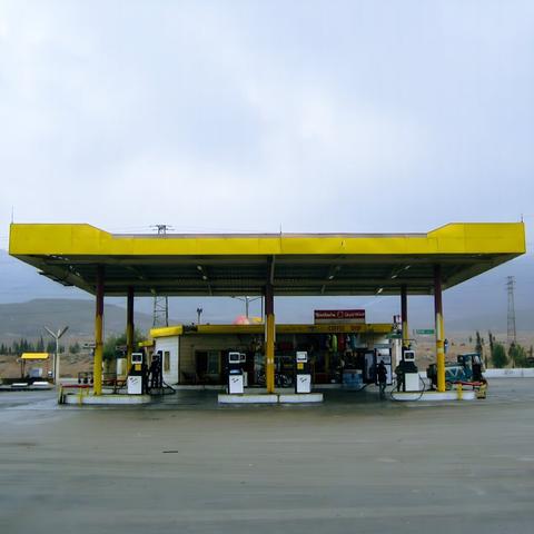 Photo of a bright yellow gas station building in front of the hills oft a desert landscape on a misty day. Nobody is around. The name of the service station is written in Arabic and Latin letters: Mandarin