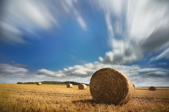 Wide angle long exposure with stretched moving clouds and a hay roll in the fields