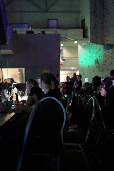 more people at computers, in the back out of focus we can see the ahk climbing wall lit up by a green spotlight