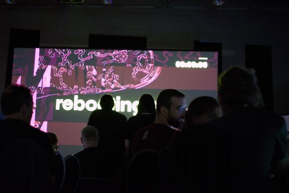 big screen says "rebooting", people are sillhouetted in front