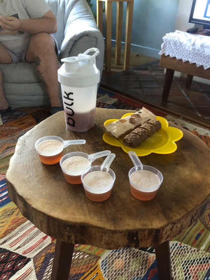 table en bois avec des cups de dosage de whey remplie de clear whey et une assiette avec une barre de whey coupée en morceaux