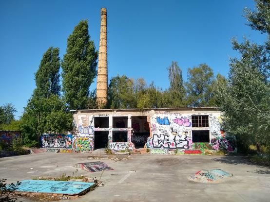 Widok na plac między zabudowaniami, przerobiony na minimalistyczny skate park. Wszystkie mury pokryte są kolorowym graffiti.

Na wprost ruina niskiej hali, z otworami w miejscach okien i drzwi, oraz jednym większym otworem, który wygląda, jakby razem z oknami wyrwano kawałek ściany. Ze szczątków poziomej belki między oknami zwisają zbrojenia. Z prawej strony w górnym oknie pozostała zardzewiała rama. Za budynkiem, po lewej stronie wysoki komin.

Obok budynku w lewo idzie mur, który następnie skręca pod kątem prostym i otacza lewą stronę placu. Powyżej muru, za budynkiem, i po prawej stronie drzewa, uginające się w prawo pod wpływem wiatru. U góry błękitne, bezchmurne niebo.