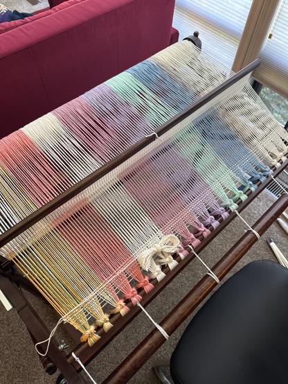 A rainbow of pastel stripes warped up on a 32” loom. A few rows have been woven at the bottom.
