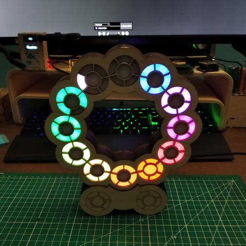 A clock stand on a desk.
Behind we can see the bottom of a sceen.

The clock case is made of laser cut wood and displays time using 72 leds.
Leds are arranged in 12 groups. Each group has one in the middle and 5 around.
The 12 groups are arranged in a circle.

It currently displays 5:49:50