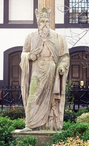 Stone statue of a crowned, broad-shouldered, bearded man. The man is of middle-age and dressed in robes.
