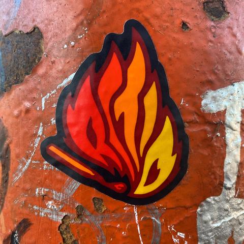 Sticker on a graffitied orange fire hydrant. It’s a burning match, in which the flames spell out “RCTID” in a red through yellow fire spectrum.