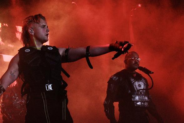 Two members of the band Hatari, performing at the Infest festival. Dressed in somewhat cyber combat gear, red stage lights enveloping them.